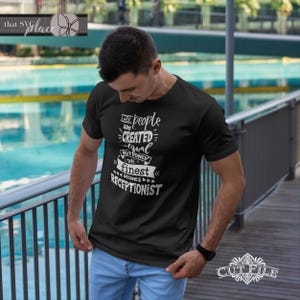Op de afbeelding: Een zwart T-shirt met witte tekst die luidt: "Alle mensen zijn gelijk geschapen, maar alleen de beste worden receptionisten".