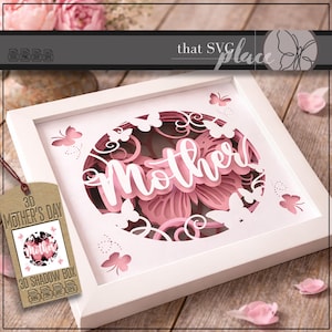 May include: A white framed 3D shadow box with a pink floral design and the word "Mother" in white script. The design includes butterflies and is accompanied by a tag that reads "3D Mother's Day".