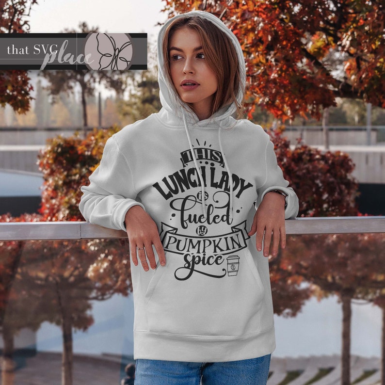 K&ouml;nnte beinhalten: Ein wei&szlig;er Hoodie mit einem schwarzen Aufdruck, der "This Lunch Lady is fueled by Pumpkin Spice" mit einem Kaffeetassen-Symbol sagt.