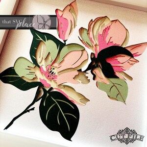 May include: A layered paper art piece featuring a detailed floral design. The artwork showcases pink, green, and cream-colored magnolia flowers with dark green leaves. The text "that SVG place" and "CUT FILE" are visible.