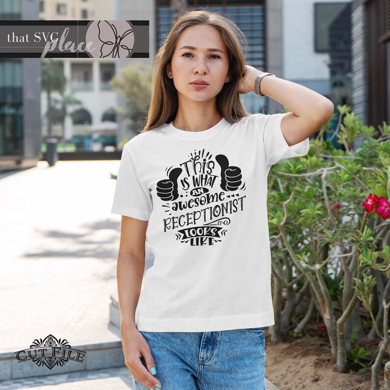 Op de afbeelding: Wit T-shirt met zwarte tekst die "Dit is hoe een geweldige receptionist eruitziet" zegt met twee duimen omhoog.