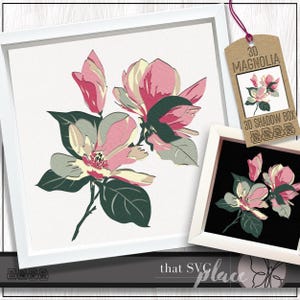 Op de afbeelding: Een ingelijste bloemenkunstprint met een magnoliabloemontwerp in roze, groen en crème kleuren. Het kunstwerk wordt gepresenteerd in een witte lijst. Een label leest "3D Magnolia 3D Shadow Box".