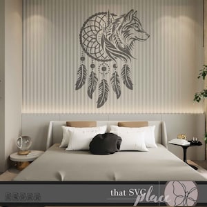 Op de afbeelding: Een zwart-wit silhouet van een wolfskop in een droomvanger met hangende veren. De droomvanger bevindt zich op een lichtgrijze muur met verticale lijnen. De afbeelding is in een slaapkamer met een bed en een nachtkastje.