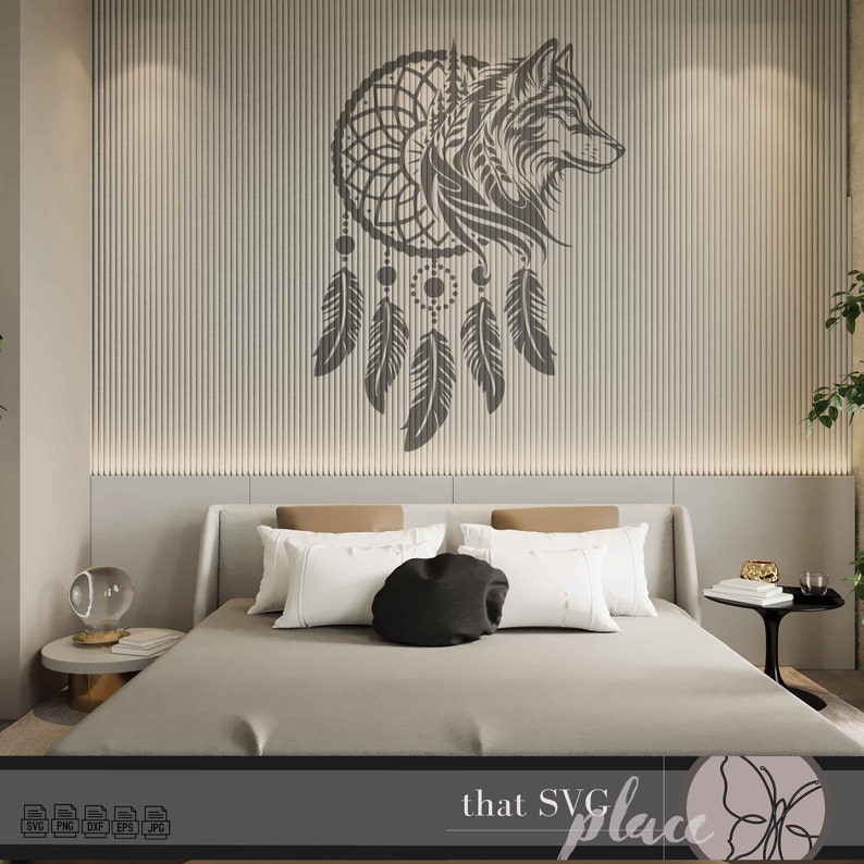 Op de afbeelding: Een zwart-wit silhouet van een wolfskop in een droomvanger met hangende veren. De droomvanger bevindt zich op een lichtgrijze muur met verticale lijnen. De afbeelding is in een slaapkamer met een bed en een nachtkastje.