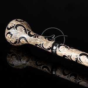 Könnte beinhalten: Ein schwarzer und cremefarbener Spazierstock mit einem dekorativen geschnitzten Design. Der Stock hat eine schwarze Kappe am Ende.