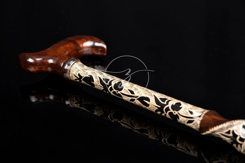 K&ouml;nnte beinhalten: Ein Gehstock aus Holz mit einem braunen Griff und einem schwarzen und wei&szlig;en Blumenmuster.