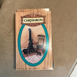 May include: A rectangular cardboard box for a Chrysnbon model kit F-260 featuring a wood-grain pattern. The front displays an oval image of a miniature black potbelly stove, a black rocking chair, a small black stool, and a black bucket with a shovel.