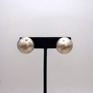 May include: A pair of silver-toned, spherical stud earrings. Each earring is a smooth, solid sphere. The earrings are displayed on a black jewelry stand against a white background. The earrings are a simple, classic design.