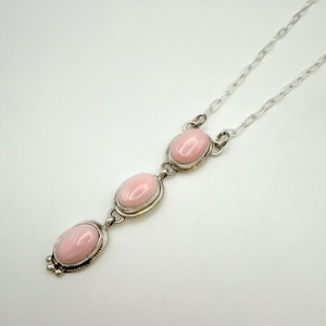 May include: A silver chain necklace with three pink oval stones. The stones are set in silver and have a smooth, polished finish.