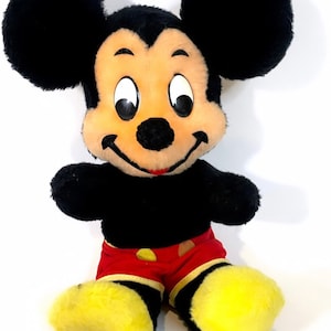 May include: A plush Mickey Mouse toy with black fur, large ears, and a red and yellow outfit. The toy has a smiling face with black eyes and a black nose.