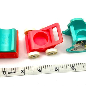 May include: Three vintage plastic Little People toys: a red and blue crib, a red stroller, and a blue rocking horse. The toys are about 2 inches tall and are in good condition.