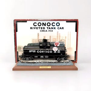 May include: A black Conoco riveted tank car model in a display case with a brown wooden base. The model is on a track and has the words "CONOCO" and "CONX 1112" printed on the side. The box has the words "CONOCO RIVETED TANK CAR CIRCA 1934" printed on it.