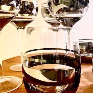 May include: Set of four clear glass wine glasses with black and silver stripes. The glasses are on a wooden surface.