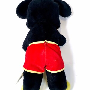May include: Black plush toy with yellow feet and red shorts. The toy has a black face and large ears.