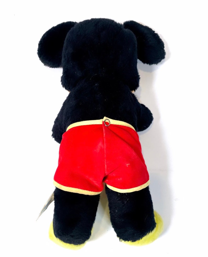 May include: Black plush toy with yellow feet and red shorts. The toy has a black face and large ears.