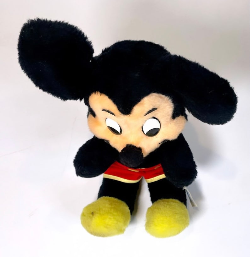 May include: A black plush Mickey Mouse toy with yellow shoes and red shorts. The toy has a classic Mickey Mouse design with large ears and a friendly face.