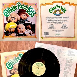 May include: A vintage vinyl record album cover featuring Cabbage Patch Kids dolls. The cover is yellow with a green title, "Cabbage Patch Kids". The album is titled "Cabbage Patch Dreams" and features 10 original Cabbage Patch songs.