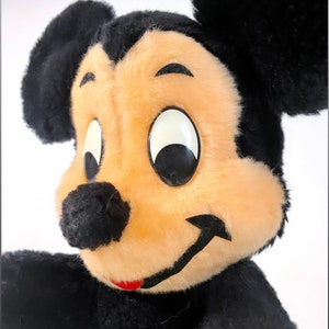 May include: A vintage plush Mickey Mouse toy with black fur, large black ears, and a smiling face with black eyes and a red mouth.