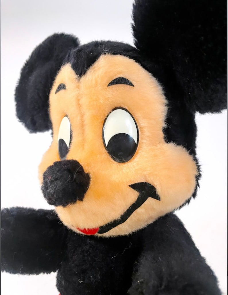 May include: A vintage plush Mickey Mouse toy with black fur, large black ears, and a smiling face with black eyes and a red mouth.
