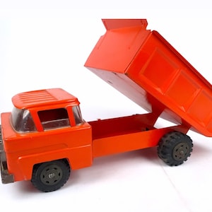 May include: Orange toy dump truck with a raised bed and black wheels. The truck has a clear plastic windshield and a detailed cab.