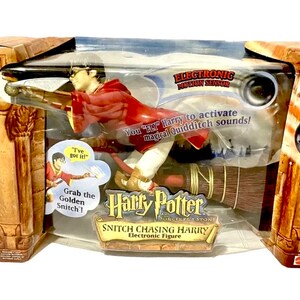 May include: Harry Potter and the Sorcerer's Stone Snitch Chasing Harry Electronic Figure toy. The figure is red and white and is holding a golden snitch. The figure is on a broomstick and has a motion sensor that activates Quidditch sounds.