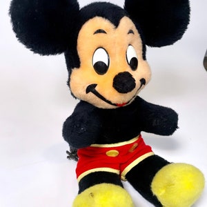 May include: A vintage plush Mickey Mouse toy with black fur, yellow shoes, and red shorts. The toy has a classic design with large ears and a friendly smile.