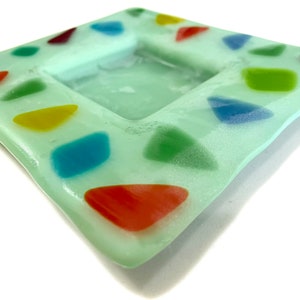 Op de afbeelding: Een lichtgroene vierkante schaal met een verzonken midden. De schaal is versierd met kleurrijke, onregelmatige vormen.