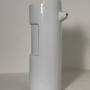 Può includere: Una brocca in ceramica bianca con corpo cilindrico, bordo superiore piatto e un piccolo beccuccio sporgente sul lato. Il recipiente presenta un pannello rettangolare incassato sul lato, creando una superficie liscia e uniforme.