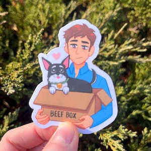 May include: A sticker featuring an illustration of a person holding a cardboard box labeled "BEEF BOX". A small black and white dog with a green collar is in the box. A pink heart is above the person's head.
