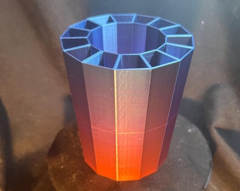 May include: A 3D printed red and blue gradient pen holder with a 16-sided design. The holder is sitting on a black circular base.
