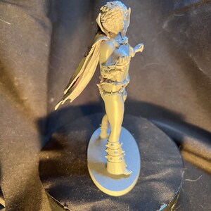 Op de afbeelding: Een grijze figuur van een krijger met een cape, harnas en stekelige accenten. De figuur staat op een ovale basis. De krijger poseert met een zwaard in de hand, klaar voor de strijd. De figuur is gemaakt van een stevig materiaal.