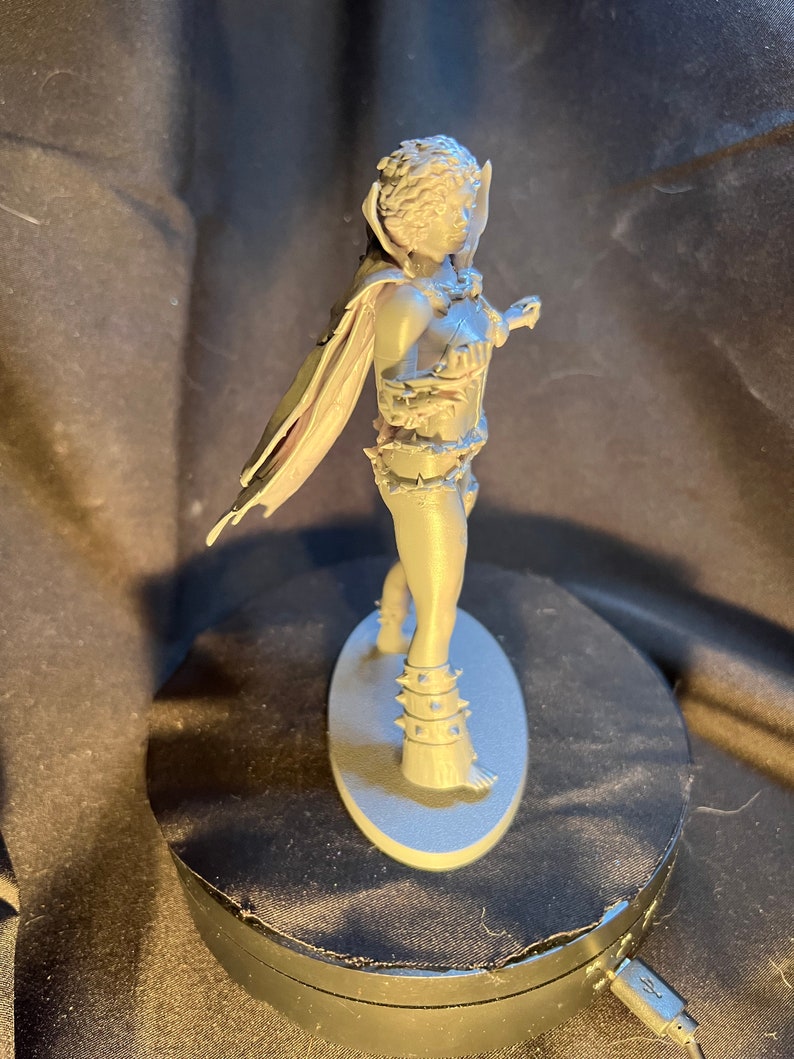 Op de afbeelding: Een grijze figuur van een krijger met een cape, harnas en stekelige accenten. De figuur staat op een ovale basis. De krijger poseert met een zwaard in de hand, klaar voor de strijd. De figuur is gemaakt van een stevig materiaal.