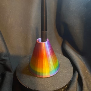Op de afbeelding: Een regenboogkleurige, 3D-geprinte standaard met een zwarte stylus die bovenop rust. De standaard staat op een zwarte ronde basis met een USB-kabel die aan de zijkant is aangesloten.