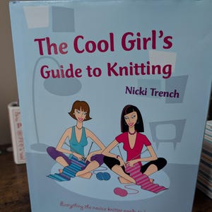 May include: A light blue book titled "The Cool Girl's Guide to Knitting" by Nicki Trench. The cover features illustrations of two women knitting. The text "Everything the novice knitter needs to know" is also on the cover.