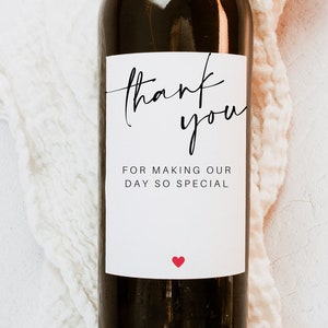 May include: A white wine bottle label with black calligraphy that reads "thank you" and "FOR MAKING OUR DAY SO SPECIAL". A small red heart is at the bottom of the label.