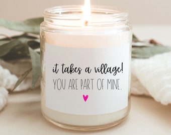 May include: A white candle in a glass jar with a label that reads "it takes a village! YOU ARE PART OF MINE." with a pink heart.