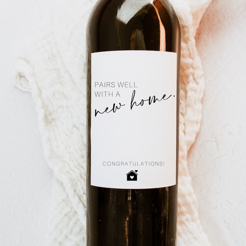 May include: A white wine bottle label with black text that reads "Pairs well with a new home." and "Congratulations!" with a small house icon below the text.
