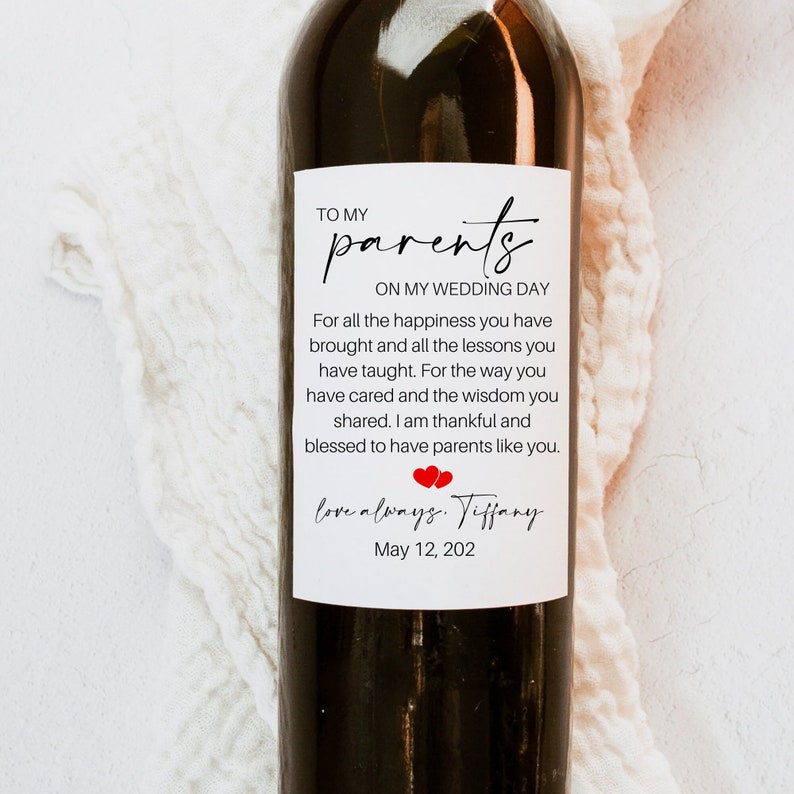 May include: A white wine bottle label with a message to parents on their child's wedding day. The label reads "To my parents on my wedding day. For all the happiness you have brought and all the lessons you have taught. For the way you have cared and the wisdom you shared. I am thankful and blessed to have parents like you. Love always, Tiffany. May 12, 202".