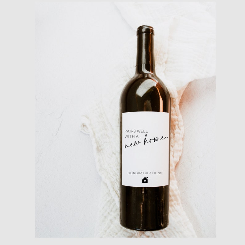 May include: A bottle of red wine with a white label that says "Pairs well with a new home. Congratulations!" and a small house icon.