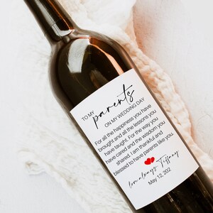 May include: A white wine bottle label with a handwritten message to parents on their wedding day. The message reads "To my parents, On my wedding day, For all the happiness you have brought and all the lessons you have taught. For the way you have cared and the wisdom you shared. I am thankful and blessed to have parents like you. Love always, Tiffany, May 12, 202".