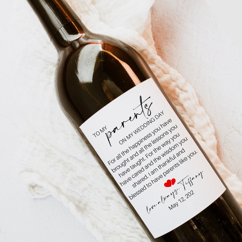 May include: A white wine bottle label with a handwritten message to parents on their wedding day. The message reads "To my parents, On my wedding day, For all the happiness you have brought and all the lessons you have taught. For the way you have cared and the wisdom you shared. I am thankful and blessed to have parents like you. Love always, Tiffany, May 12, 202".