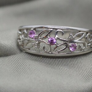 Puede incluir: Un anillo de plata con un delicado diseño floral y tres piedras preciosas rosas.