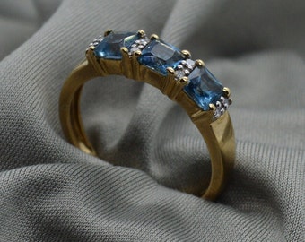 Puede incluir: Un anillo de banda de oro con cuatro piedras preciosas de topacio azul y pequeños diamantes engastados en la banda.