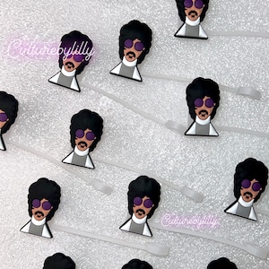 May include: A set of 10 purple and black Prince-inspired shoe charms. Each charm features a cartoon image of Prince wearing a purple suit and sunglasses. The charms are attached to clear plastic strings.