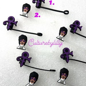May include: A set of eight purple and black Prince-themed charms. Each charm features a purple symbol and a cartoon image of Prince wearing sunglasses. The charms are attached to black cords with a loop at the end.