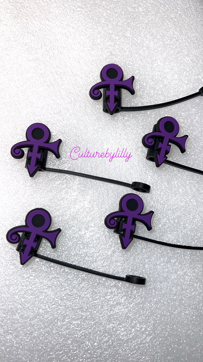 May include: Five purple Prince symbol charms on black elastic bands. The charms are attached to the bands with a small black ring.