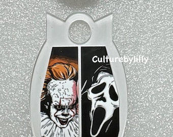 May include: A white oval-shaped keychain with a graphic of Pennywise the clown from the movie "IT" on the left side and Ghostface from the movie "Scream" on the right side. The keychain has a hole at the top for attaching to a key ring. The text "Culturebylilly" is printed on the right side of the keychain.