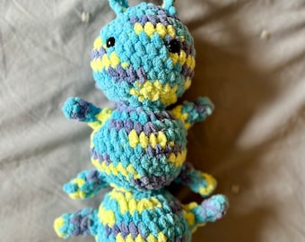 May include: A crocheted plush toy shaped like an ant with a blue, yellow, and purple color scheme. The ant has a segmented body and black eyes.