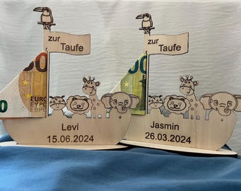 Könnte beinhalten: Zwei Holzboote mit Tierfiguren, einer Giraffe, einem Elefanten und einem Löwen, und dem Text "zur Taufe" auf einer Flagge. Die Boote sind mit einem 50-Euro-Schein verziert. Das erste Boot trägt den Namen "Levi" und das Datum "15.06.2024". Das zweite Boot trägt den Namen "Jasmin" und das Datum "26.03.2024".
