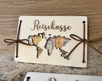 Könnte beinhalten: Eine weiße Holzkiste mit einem Ausschnitt einer Weltkarte und dem Text "Reisekasse" auf der Vorderseite. Die Kiste ist mit braunen Lederbändern gebunden.